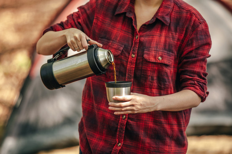A Lady pouring monster buck coffee from a thermos into a coffee lid wear a plaid camping shirt